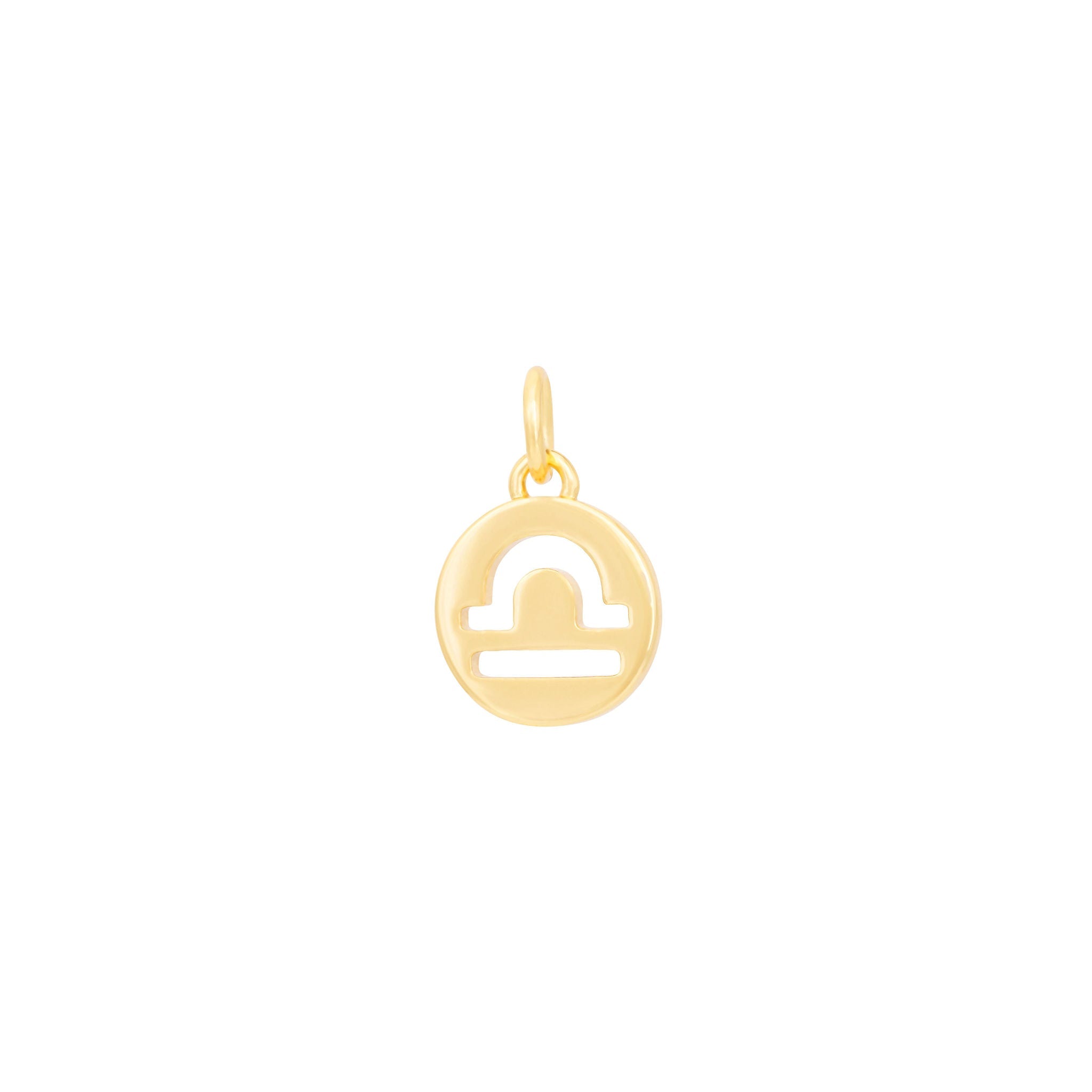 The Libra Charm - Gold by The Ends features a simple, stylized scale icon representing the Libra zodiac symbol. This circular piece of Zodiac sign jewelry includes a small loop at the top for easy attachment to a necklace or bracelet. The minimalist and elegant design makes it perfect for medallion charm collections.